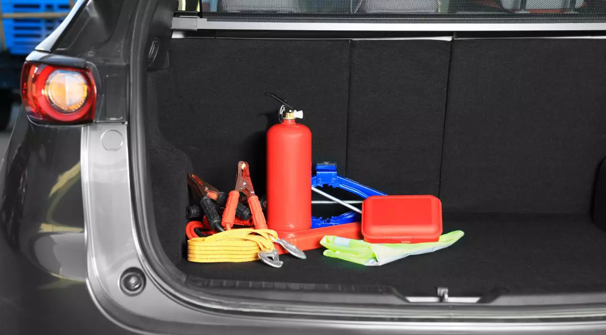 Triunghi reflectorizant, stingător de culoare roșie, cric roșu și alte obiecte în portbagajul unei mașini