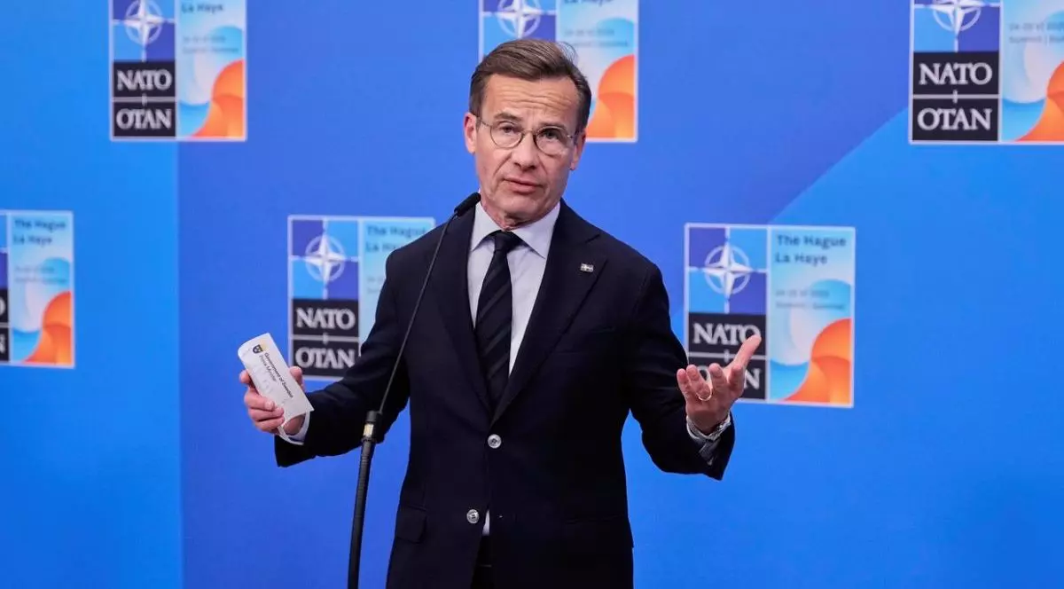 Prim-ministrul Suediei, Ulf Kristersson, in costum inchis la culoare, camasă albă si cravata, surprins cu mainile larg deschise, cu o hartie mică in mana dreapta, în timp ce vorbește cu presa la sosirea sa la summitul NATO de la Haga, Olanda, miercuri, 25 iunie 2025.