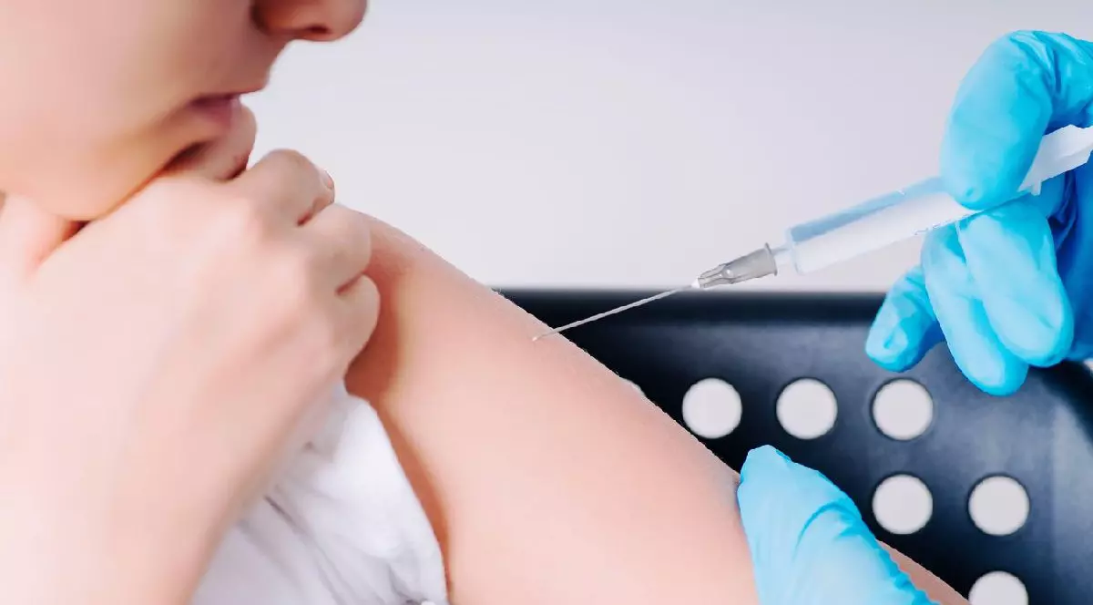 Un copil este vaccinat în mână de un cadru medical care poartă mănuși de plastic albastre