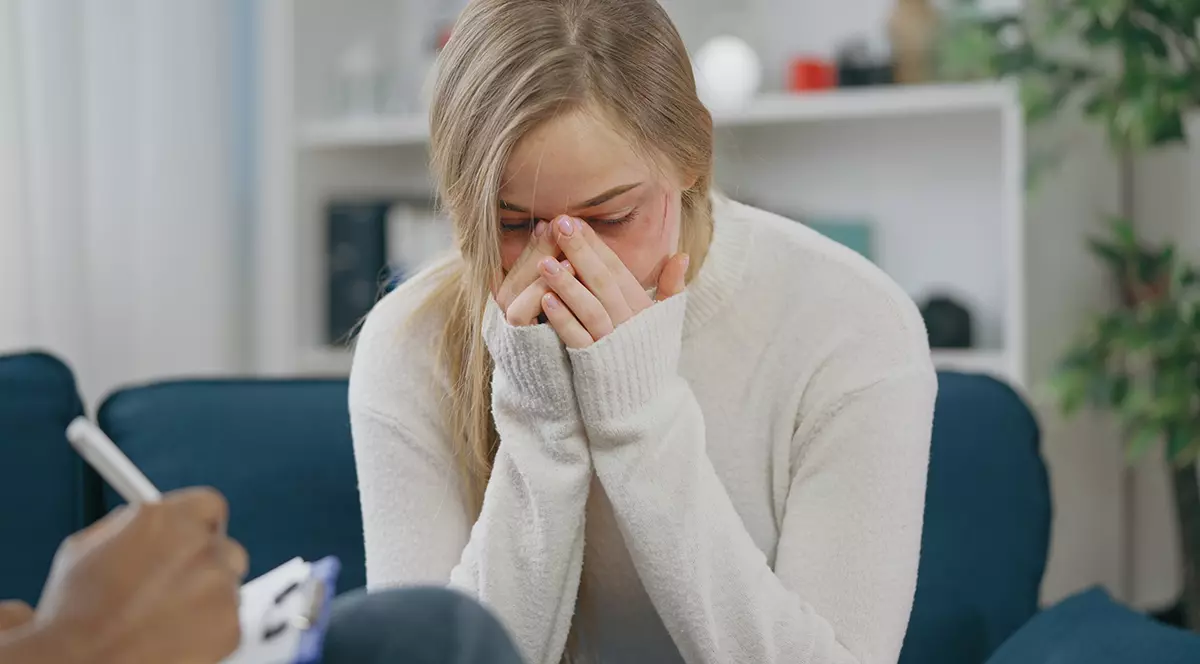 Tânără victimă a violenței domestice plângând la o ședință de terapie, având nevoie de sprijin emoțional. Foto ilustrativ