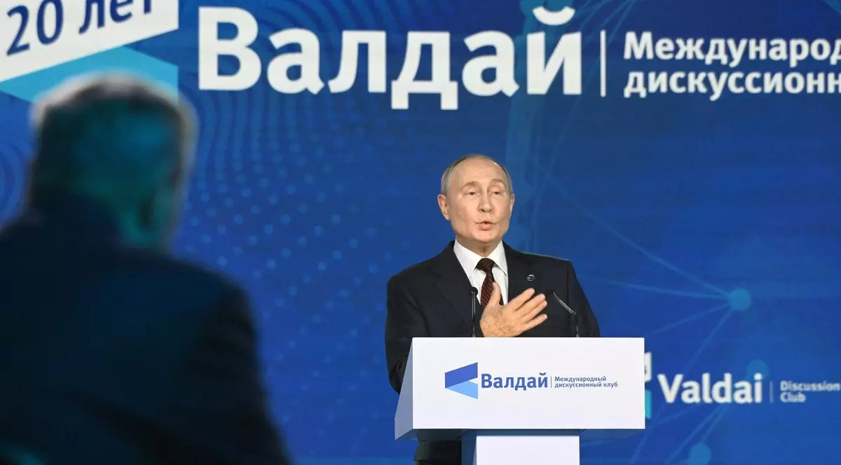 Președintele rus Vladimir Putin luând cuvântul la pupitru în cadrul ședinței a celei de-a XXI-a reuniuni anuale a clubului internațional de discuții „Valdai”. Putin este imbracat intr-un costum negru, camasa alba si cravta, iar in spatele lui se observa un panou urias cu numele clubului Valdai