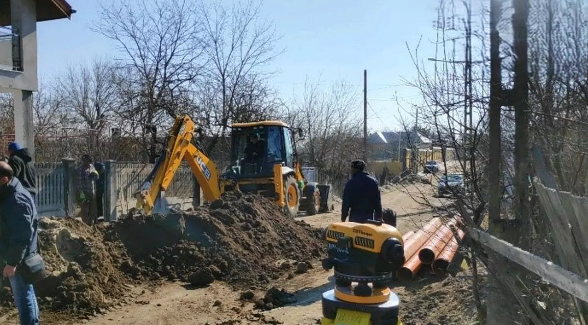 Un excavator sapă o groapă pe o stradă din comuna Cotnari pentru extinderea rețeleui de apă, mai 2024