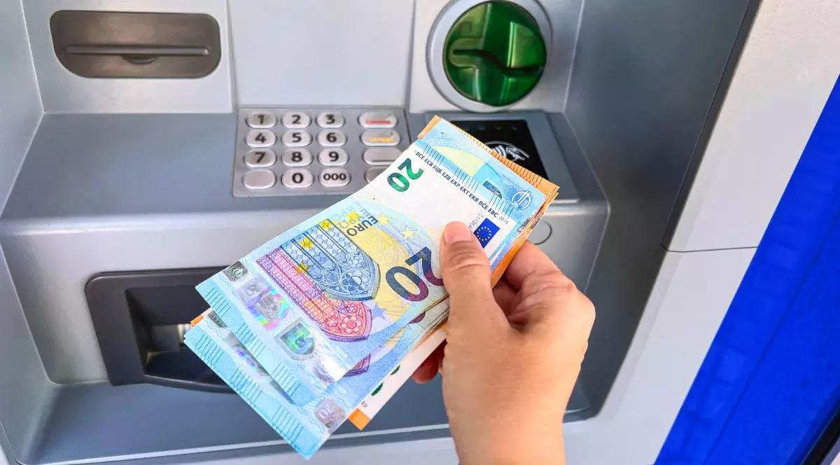 Bancnote de 20 și 50 de euro ținute într-o mână în fața unui bancomat