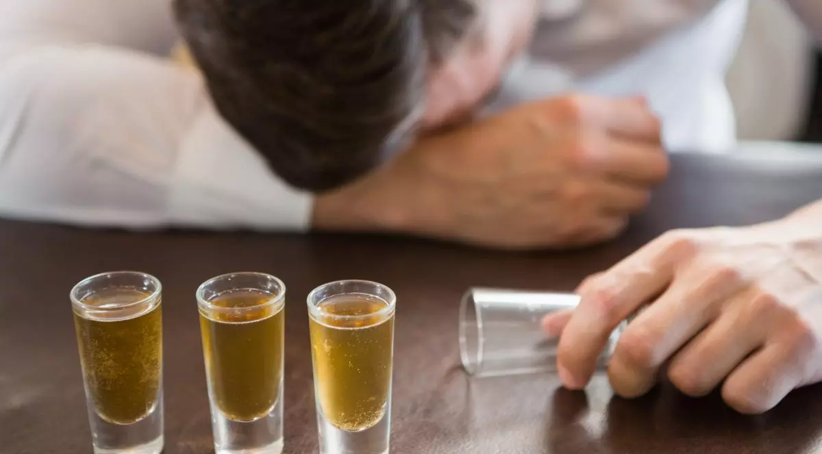 Un bărbat în costum doarme cu capul pe bar după ce a băut. Mai multe shoturi sunt în fața lui