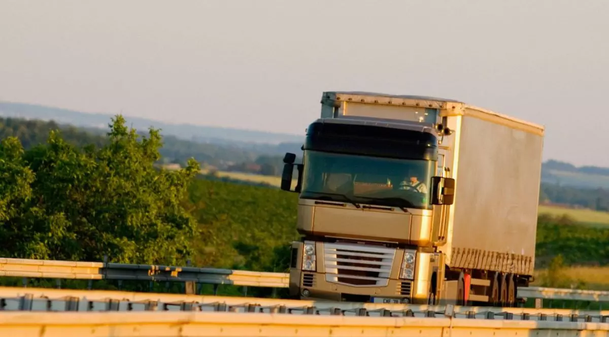 Un camion cu remorca în timp ce se deplaseaza pe un drum in Franța, pe marginea drumului se vad arbusti