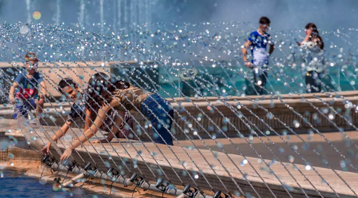 Mai mulți bucureșteni în timp ce încearcă să se răcorească băgând mâna în apa unei fântâni de la Unirii