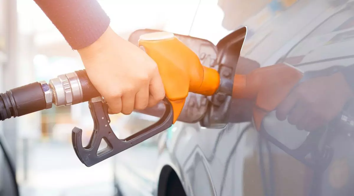 Un bărbat ține în mână o pompă portocalie și alimentează cu carburanți o mașină gri, în Thailanda