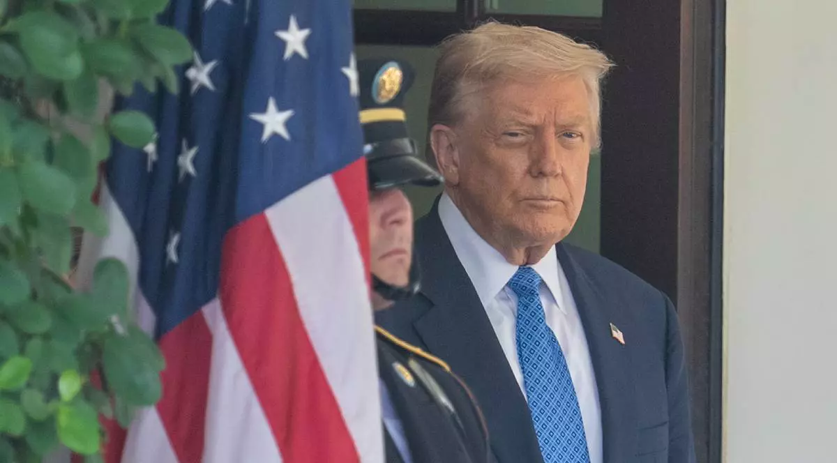 Președintele american Donald Trump la Casa Alba, acesta stă la intrare și este supărat, poartă un costum albastru, iar în stânga pozei se vede steagul SUA