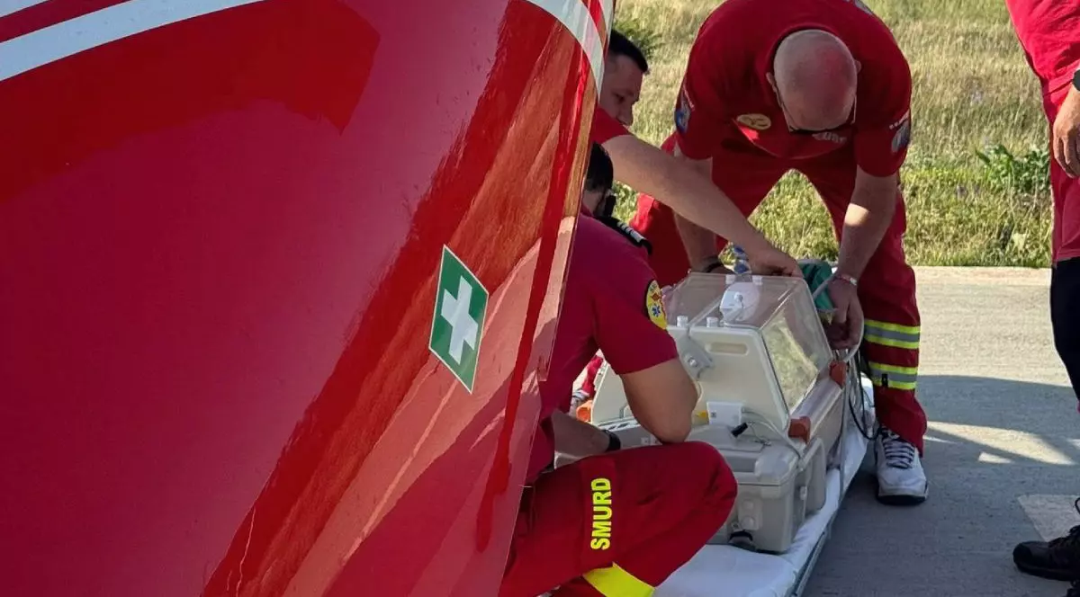 In imagine un echipaj SMURD cu trei medici, imbracați in echipament rosu, stau langa incubator in care este un bebelus nou nascut