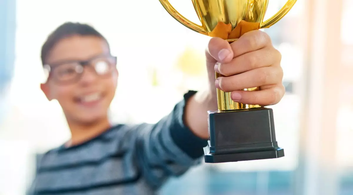 Copil cu ochelari care ține în mână o cupă și râde fericit