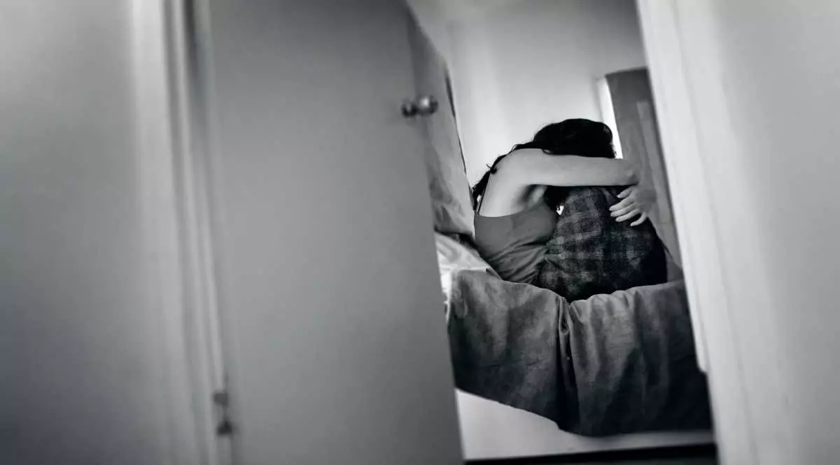 Femeie traumatizată. Ea stă pe un pat într-un dormitor