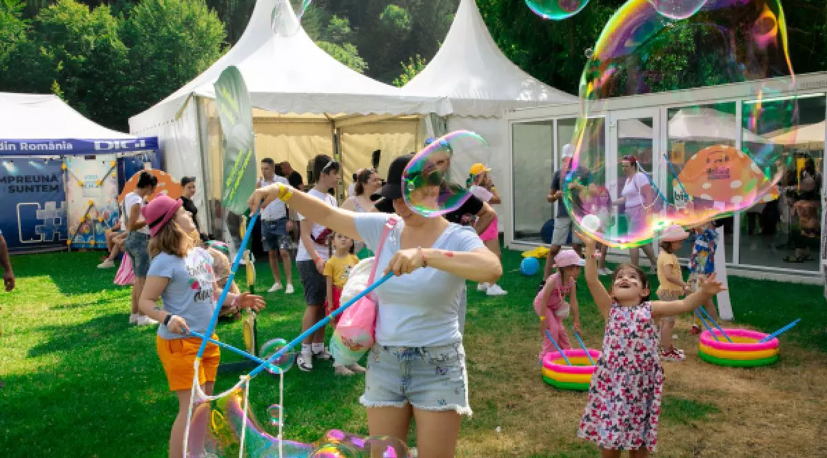 O fetiță și o femeie adultă fac baloane de săpun ajutându-se de niște bețe