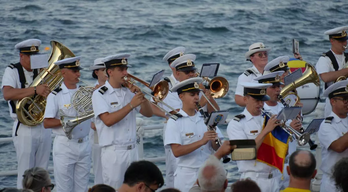 Militarii din cadrul Forțelor Navale Române în timpul concertului de luni seara de pe faleza Cazinoului din Constanța, aceștia poartă uniforme albe și cântă la instrumente muzicale, țin steagul României în mână