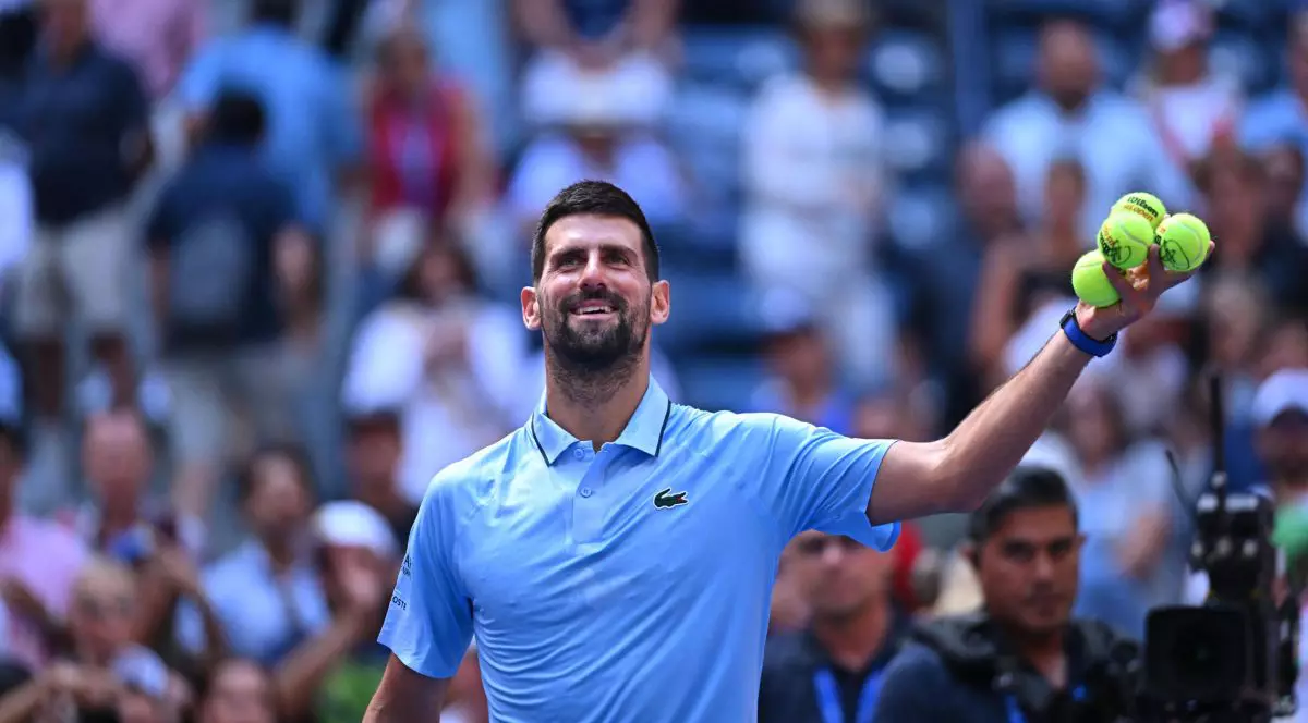 Novak Djokovic zâmbește pe terenul de la US Open, în timp ce ține în mâna stângă patru mingi de tenis, august 2025