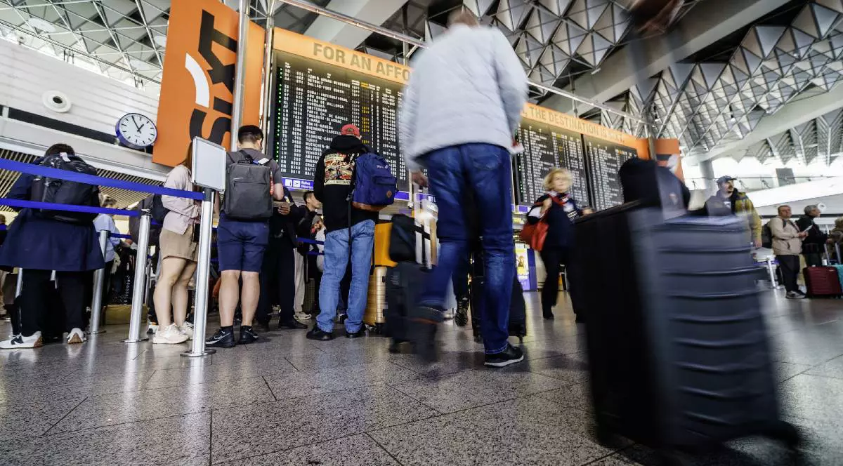 Mai mulți pasageri stau la coadă să urmărească afișajul întârzierilor dintr-un aeroport german.