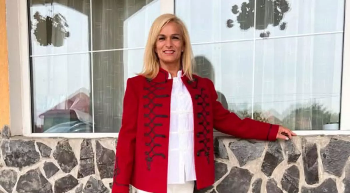 Campioana Judit Palecian, in tunica rosie cu model negru si o camasa alba, in fata unei case