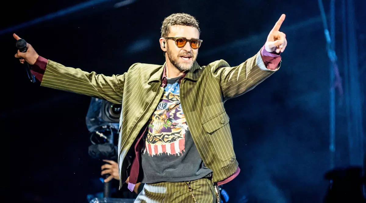 Justin Timberlake, pe scenă, în timpul unui concert, cu microfonul în mână, îmbrăcat cu un compleu verde
