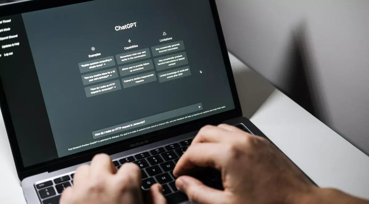 Imagine cu un laptop și cu mâinile unui bărbat pe tastatură. Pe ecranul dispozitivului este afișată aplicația ChatGPT