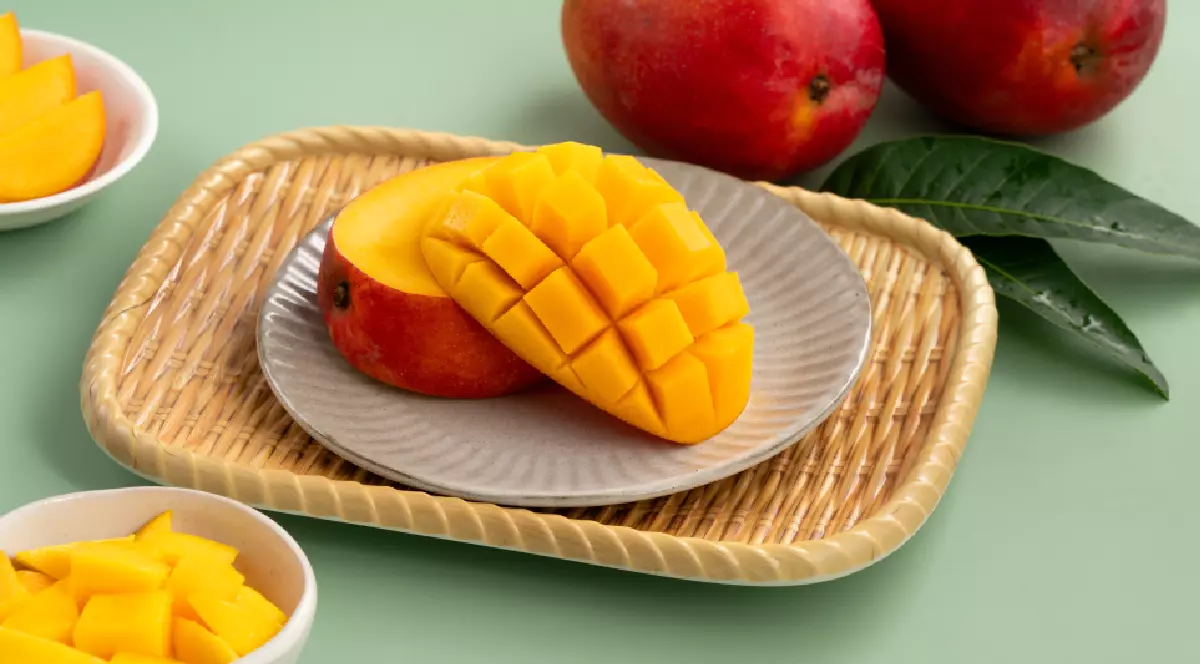 Cuburi suculente de mango galben cu mango întreg pe un fundal de masă verde.