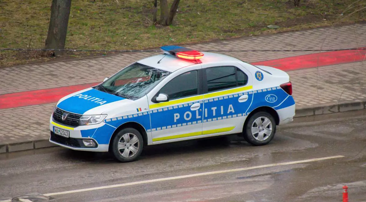 O mașină de Poliție, în timpul unei intervenții la fața locului, are girofarurile pornite și se deplasează pe stradă