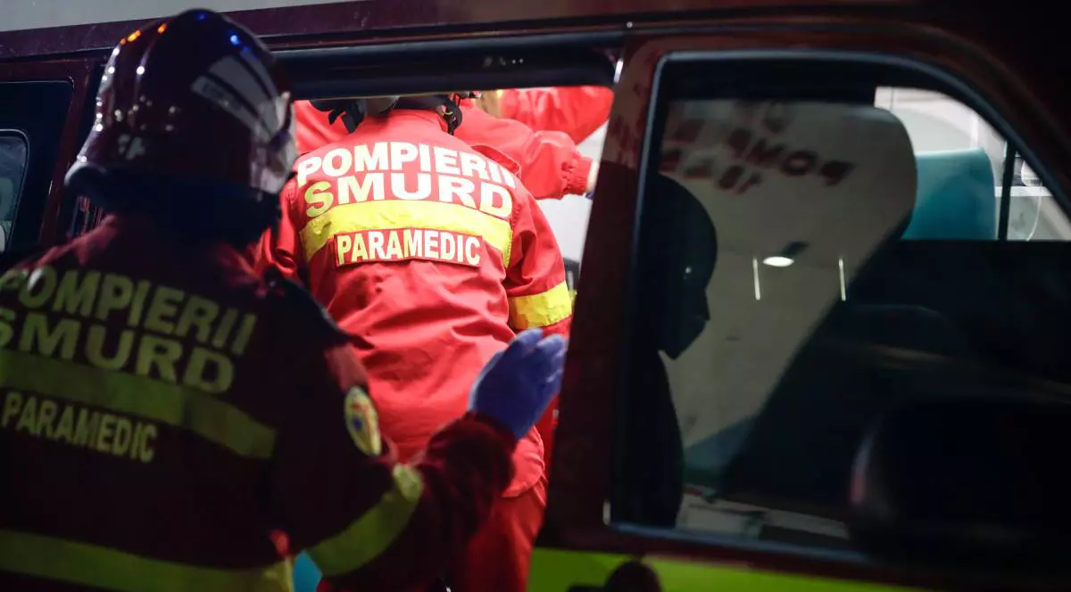 Doi medici din echipajul SMURD în timp ce intră în ambulanță, aceștia poartă căști pe cap și uniforme roșii