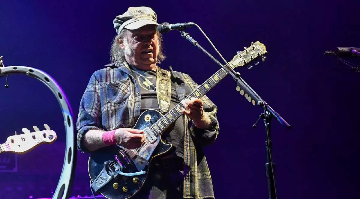 Cântărețul Neil Young ține o chitară în mână și cântă la un microfon la un festival