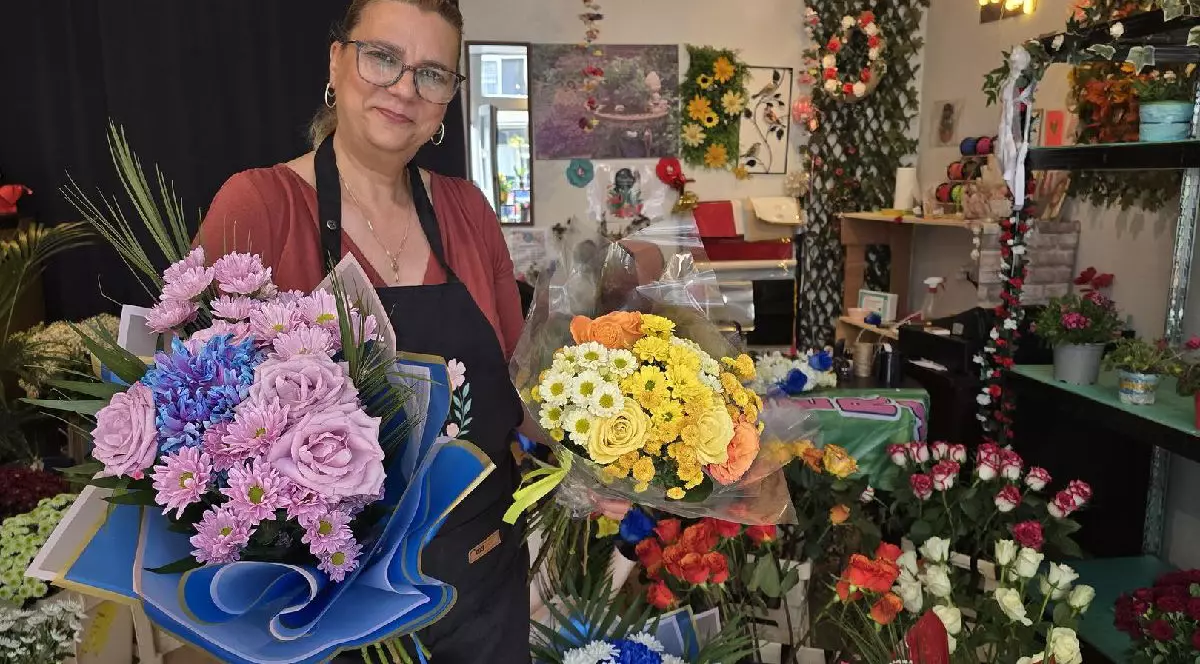 O femeie ține două buchete de flori într-o florărie
