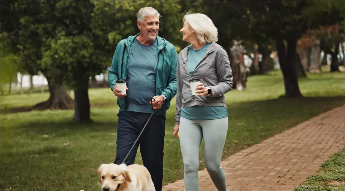 Doi oameni care se plimbă cu un câine în parc