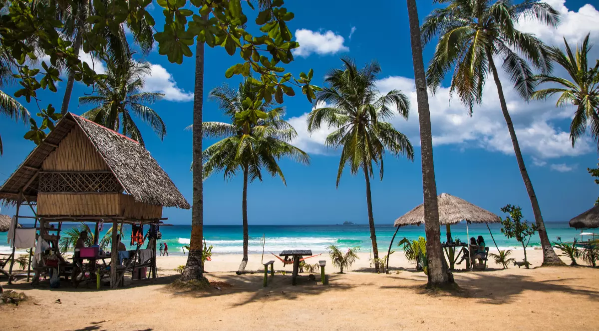 Plajă tropicală în Palawan, Filipine, cu nisip alb, palmieri, bungalouri tradiționale și apă turcoaz