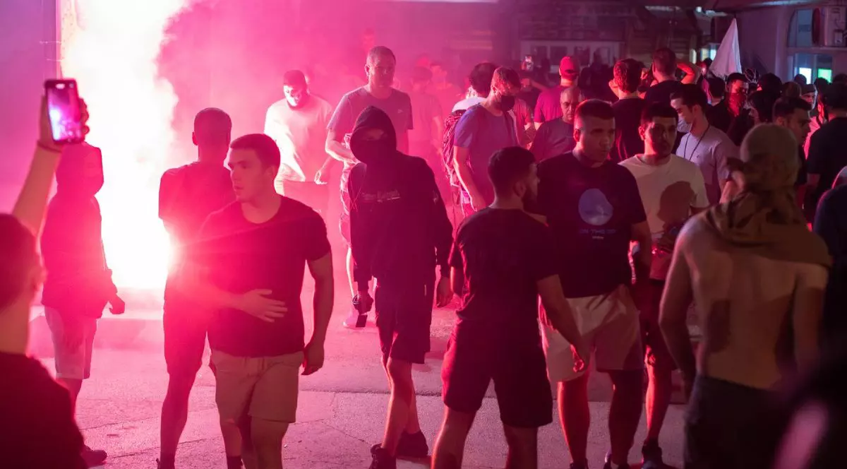 Zeci de tineri, îmbrăcați în tricouri și pantaloni, noaptea, pe o stradă din Novi Sad, cu torțe aprinse pe fundal