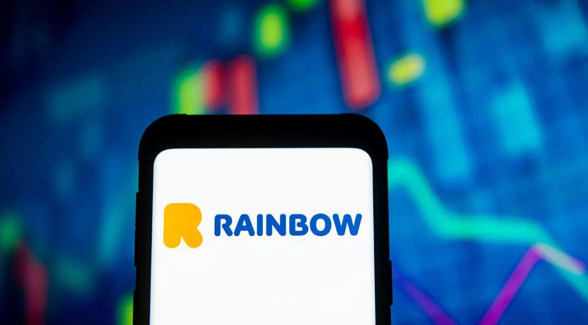 logo-ul companiei de turism Rainbow Tours, afișat pe ecranul unui telefon mobil, cu cotatii bursiere pe fundal