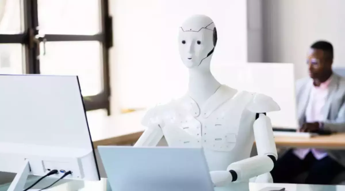 Un robot umanoid aflat la birou, în timp ce lucrează pe laptop