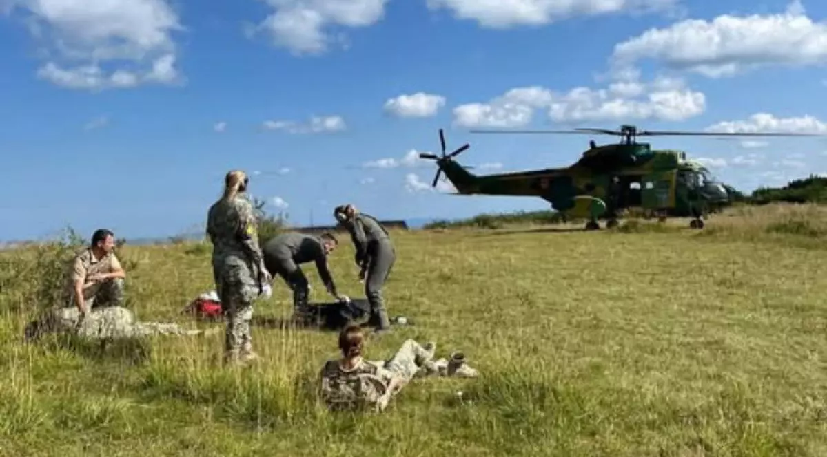 In imagine un elicopter al MApN aterizat pe o zona cu iarba, se vad 5 persoane, unii militari ai fortelor aeriene romane