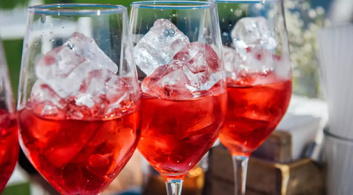 Se pune gheață în vin? Câteva pahare de vin umplute cu gheță și vin roze si puse pe un bar la o petrecere în aer liber