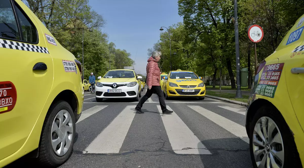 O femeie cu geacă roși traversează pe o trecere de pietoni, blocată de patru taxiuri - 2017
