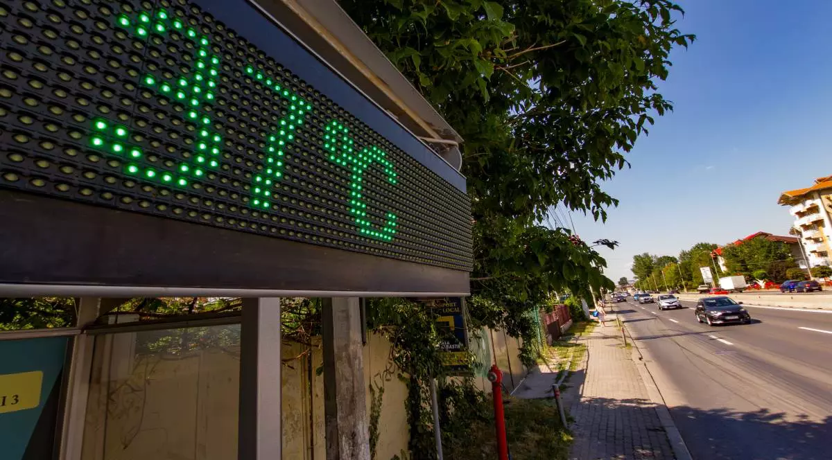 Un termometru stradal care indică temperatura de 37 de grade Celsius pe un bulevard însorit