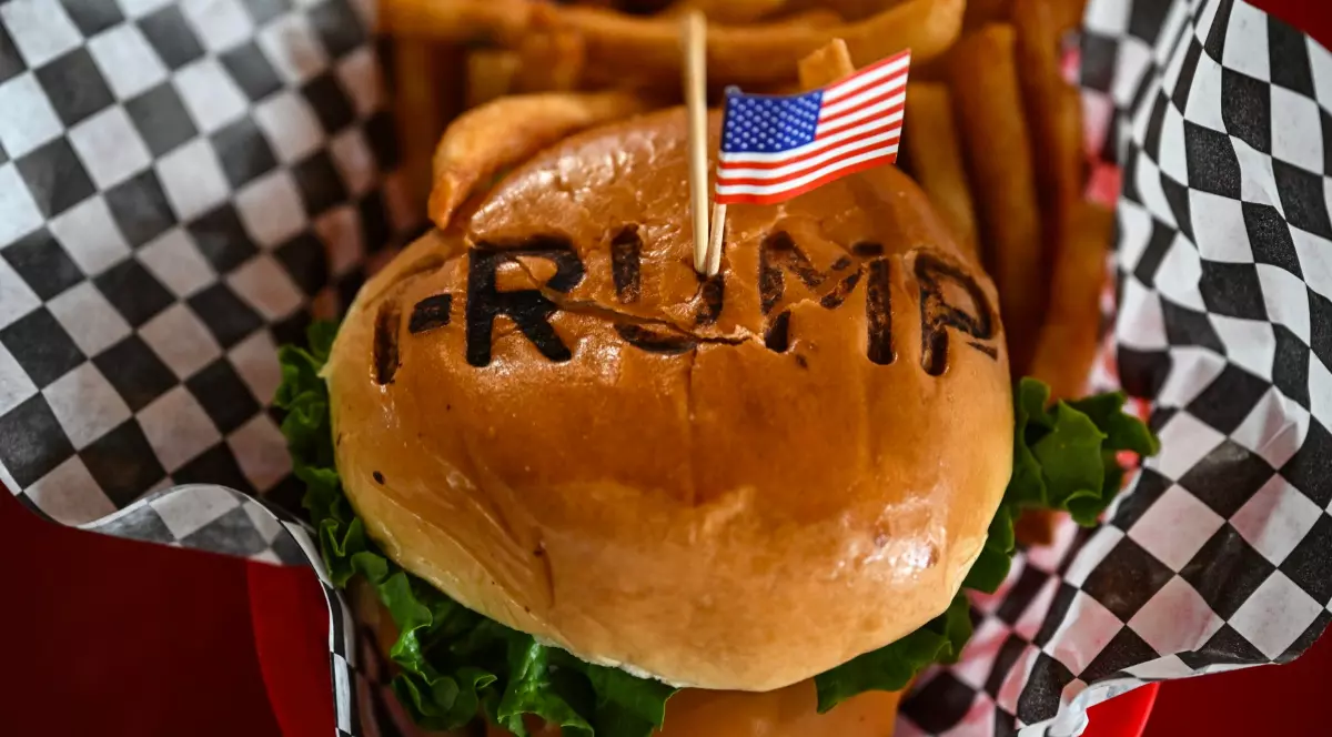 Imaginea arată un burger cu chiflă pe care este inscripționat cuvântul „TRUMP”