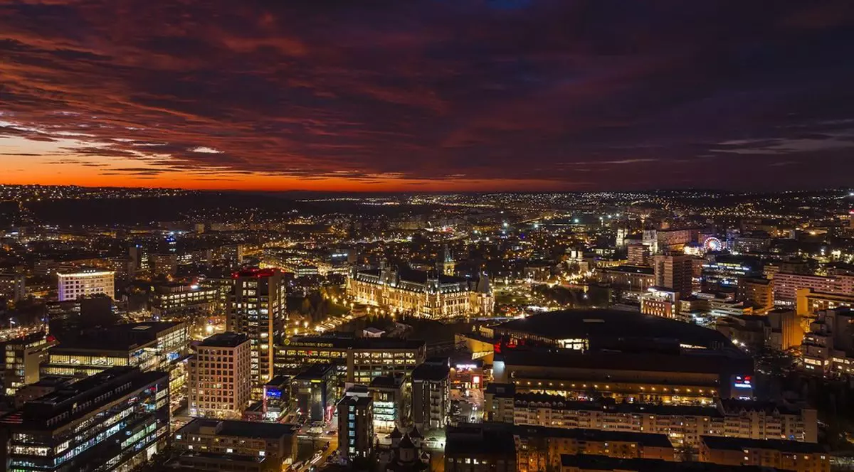 Orașul Iași văzut seara, de sus, se văd clădiri de firme și blocuri, multe luminițe galbene și cerul înnorat