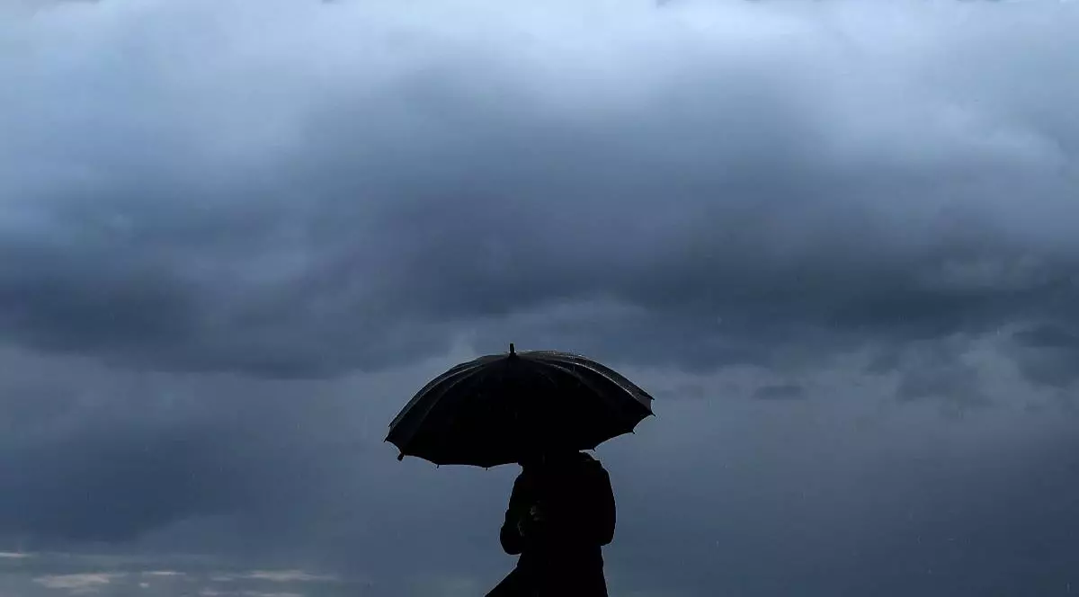 o persoană stă sub umbrelă și pe fundal se vede un nor pufos de ploaie