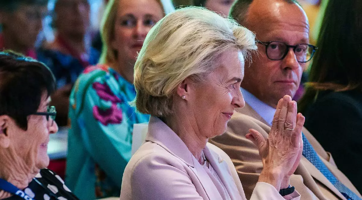 Ursula von der Leyen zâmbește, lângă Merz, care o privește consternat, la o ședință PPE