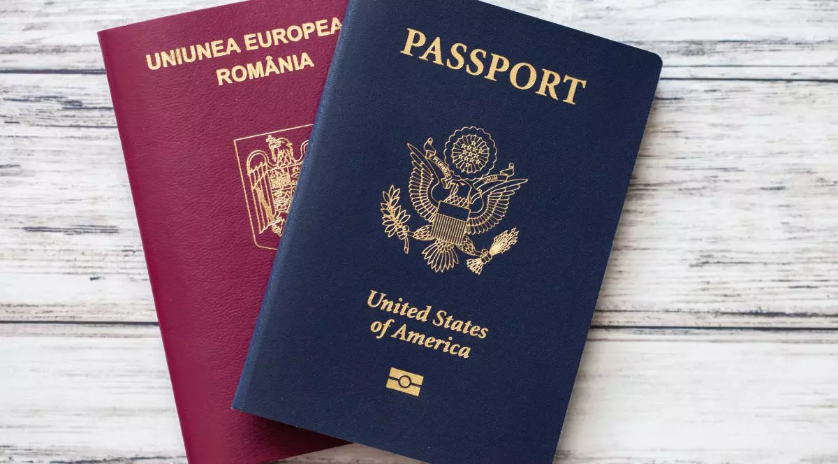 Pașapoarte americane albastre și românești roșii așezate plat pe un fundal de lemn.