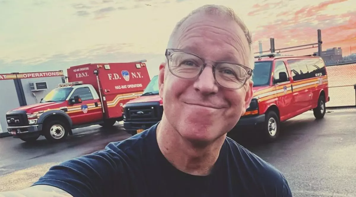 Jonathan Kleisner, milionarul care a lăsat baltă afacerile ca să devină paramedic, zâmbește având pe fundal mai multe ambulanțe, iunie 2025