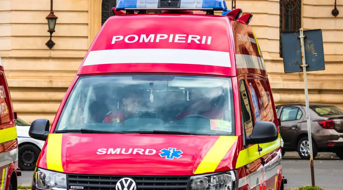 O ambulanță roșie SMURD parcată cu spatele, la volan și pe locul din dreapta al șoferului se află doi asistenți medicali care verifică niște acte