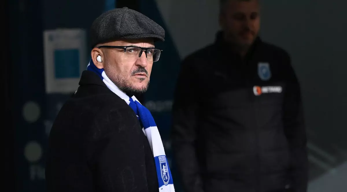 Imagine cu Adrian Mititelu. Poartă un palton negru și o eșarfă în culorile echipei FC U Craiova. Pe cap poartă o șapcă de culoare închisă