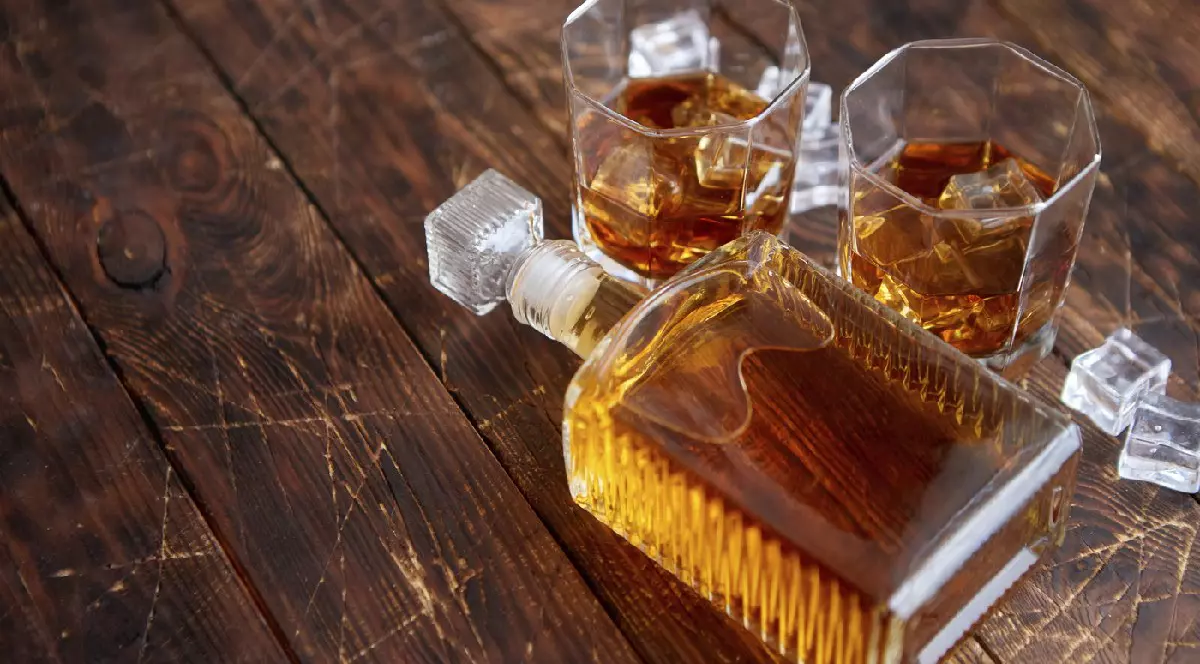 Sticlă de whisky cu două pahare așezate pe o masă rustică din lemn