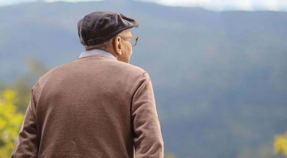 Un bătrân îmbrăcat în pulover maro, cu o bască pe cap, pozat de la spate