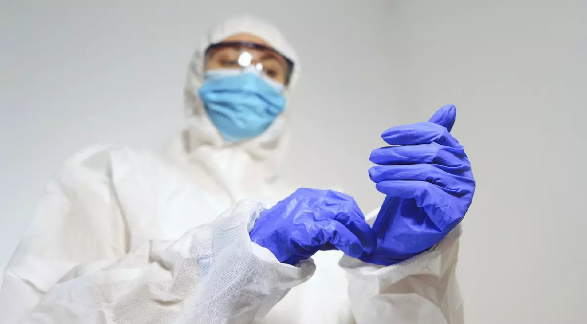 Personal medical în costum de protecție își pune mănușile