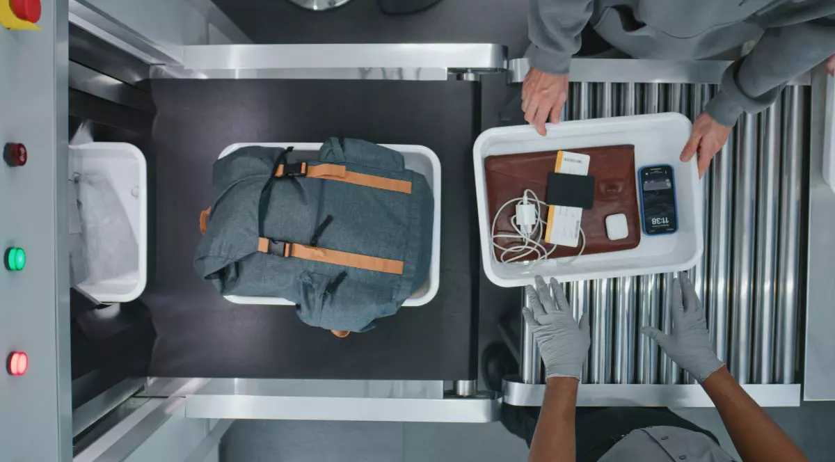 Vedere de sus cu mainile unor persoane, pasageri punând obiecte personale în tăvi de plastic pentru proceduri de screening în bandă transportoare de scanare cu raze X. Punctul de control al securității îmbarcarea în avionul de zbor