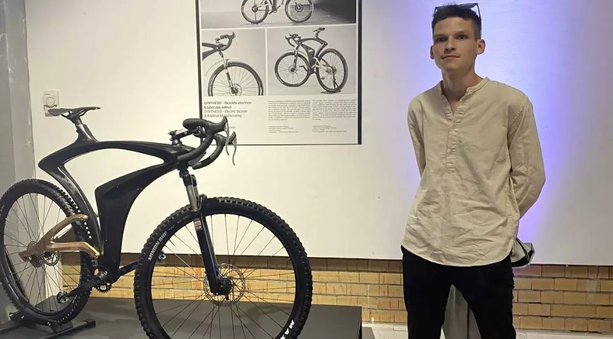 David Borovci îmbrăcat în cămașă albă și blugi negri, cu ochelari pe cap, lângă o bicicletă