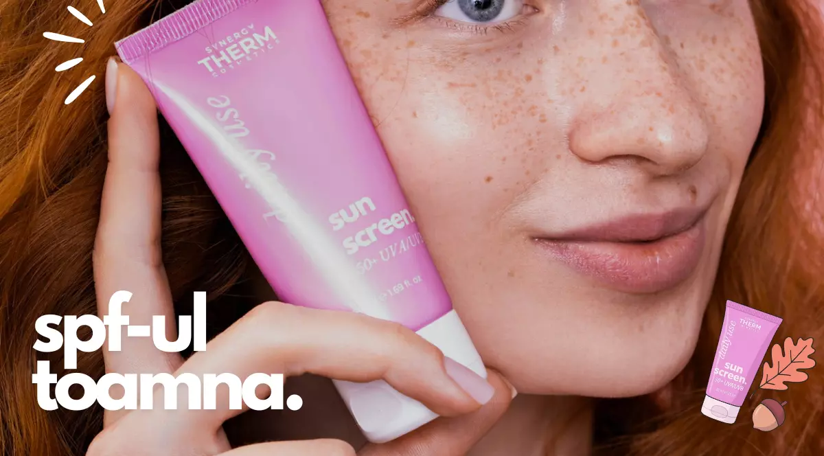 Femeie tanara, roscata, cu ochii albastri, tine in mana langa fata un tu roz de protectie solara de la Synergy Therm